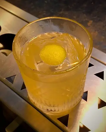Coquetel amarelo em copo baixo com casca de limão sobre o gelo