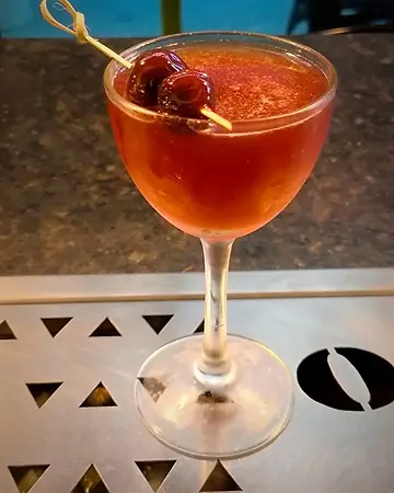 Coquetel vermelho em taça com duas cerejas no palito