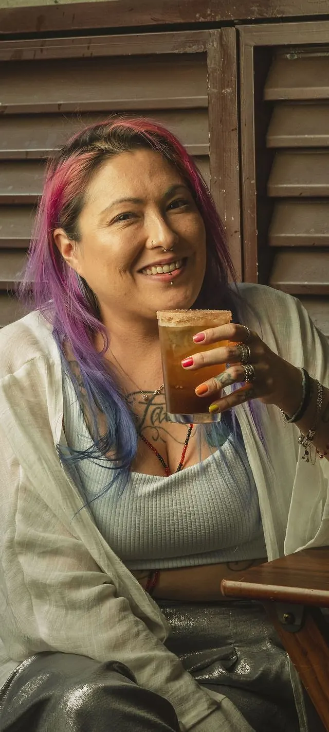 Thatta sorrindo, sentada com um coquetel na mão